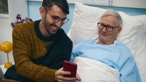 Young man shows his father a cell phone as he is lying on the bed