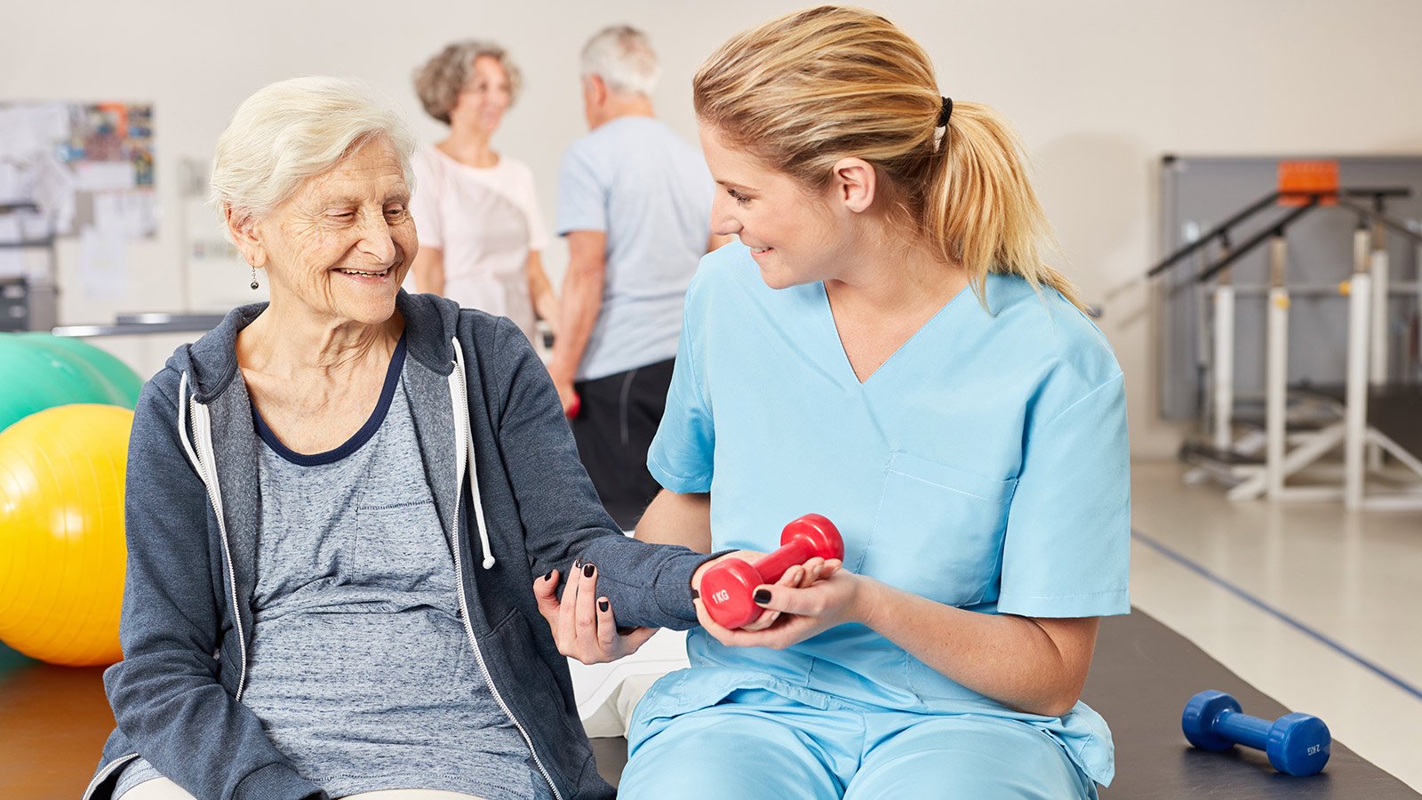 nurse helping elderly lady lift weights